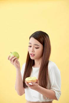 Portrait of a shocked young asian woman donut and green apple isolated over yellow background