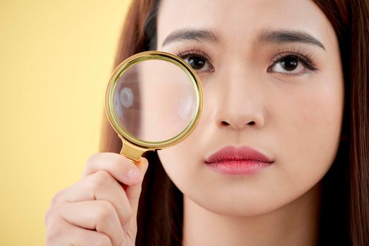 Woman with magnifying glass isolated on a yellow background