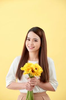 Asian lady holding a bunch of flower standing against a wall