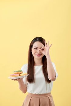 Young woman holding plate donut doing ok sign with fingers, excellent symbol