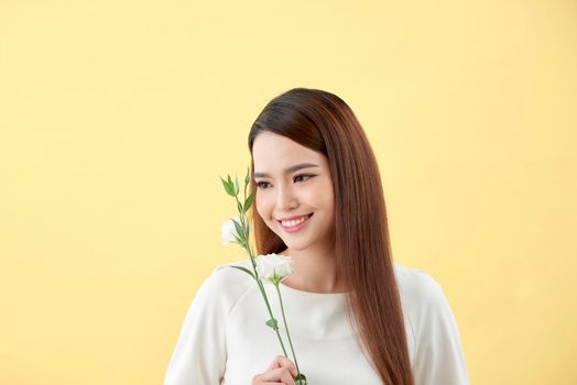 Beauty portrait of lady 20s holding white lisianthus flowers over yellow background