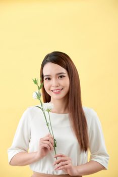 Beauty portrait of lady 20s holding white lisianthus flowers over yellow background