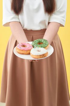 Female hands holding tasty donuts on yellow background