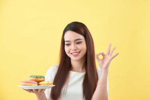 Beautiful young woman smiling holding a plate full of delicious color donuts 