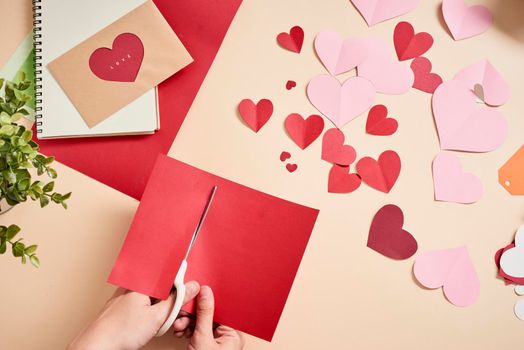 woman cuts out red felt hearts, homemade crafts for Valentine's day, hand made creativity, top view