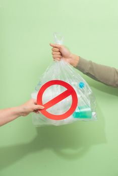 Male hand holding a waste bag isolated on green background.