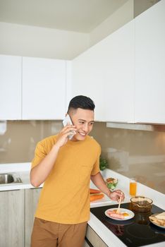 Handsome bachelor 30s talking on mobile phone, while having breakfast in morning
