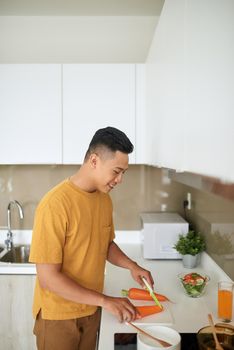 happy young man cutting vegetables in kitchen