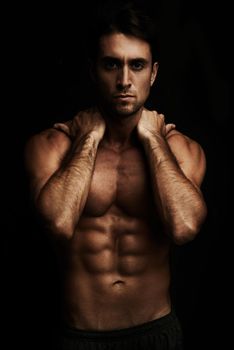 Dark and sexy. Gorgeous young man with a six pack isolated on black.
