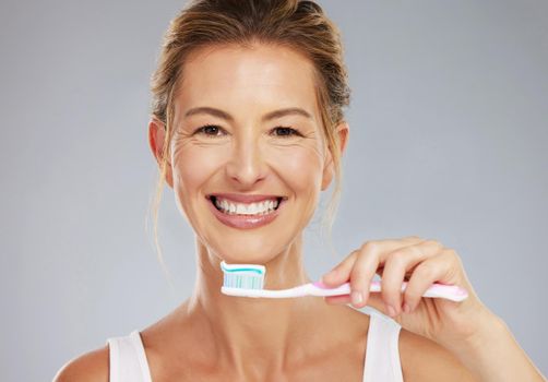 Senior woman and portrait with toothbrush for dental treatment and teeth whitening at grey studio. Mature, healthy and happy lady with toothpaste for mouth cleaning and white smile face mockup.