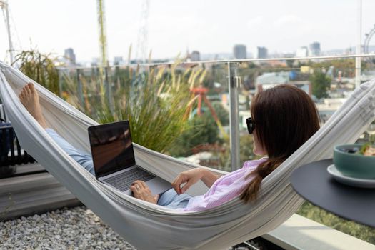 young woman freelancer working in hammock on terrace