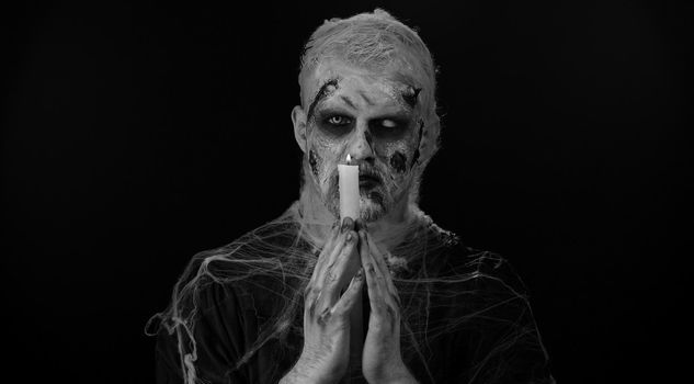 Frightening man with Halloween zombie bloody makeup spells conjures over candle, voodoo rituals