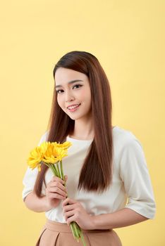 Beautiful woman in the white shirt with flowers gerbera in hands on a yellow background. She smiles and laughs
