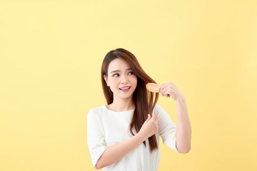 Portrait of attractive smiling woman brushing her hair isolated on yellow studio shot