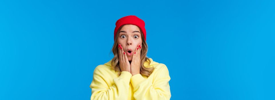 Wow incredible. Impressed and curious good-looking young girl reacting shocked and astonished to interesting awesome news, touch cheeks folding lips stunned, blue background