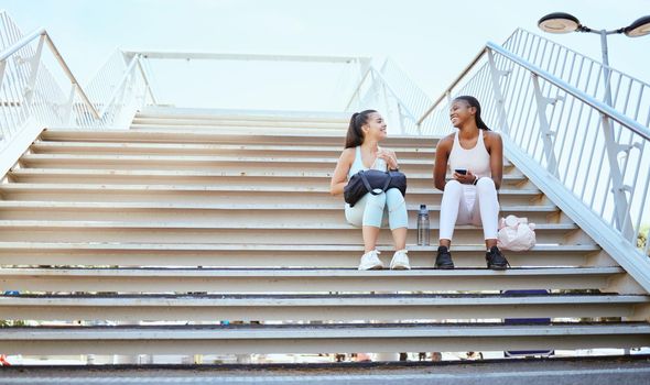 Friends, happy and relax after exercise on steps together, talking and bonding after morning cardio outdoors. Smiling, cheerful and females resting on stairs, enjoying free time after workout in city