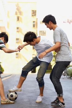 Some friendly competition. Three asian boys playing soccer in the street.