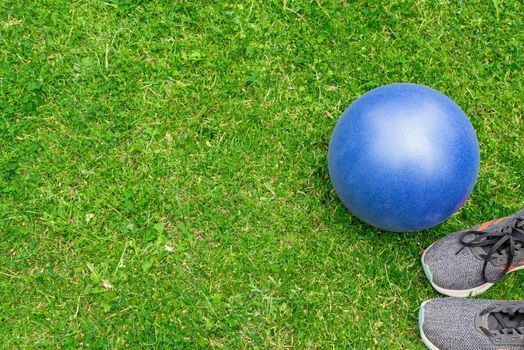 Fitness ball and sneakers on the green grass background