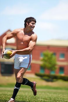 Fun in the sun. Full length shot of a shirtless young rugby player executing a pass.