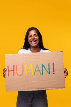 Portrait of young indian woman holding a LGTB rights cardboard poster isolated on yellow background.Studio shot.