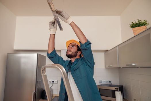 Professional electrician worker in uniform is installing electric lamps light in kitchen