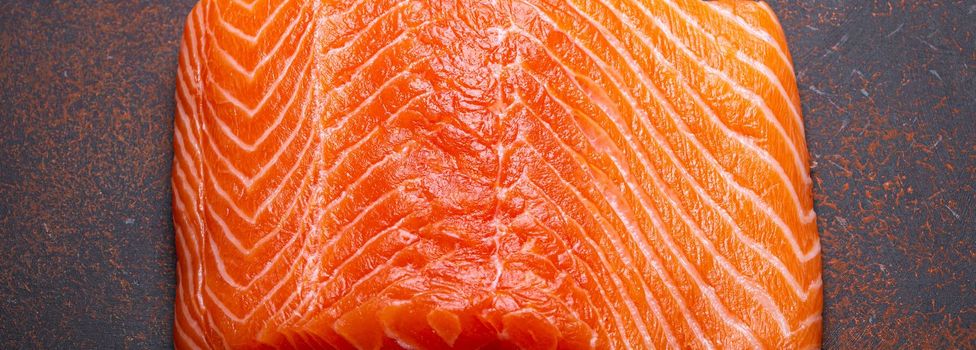 Piece of fresh Norwegian raw salmon fillet on dark brown rustic background top view, healthy nutrition and diet