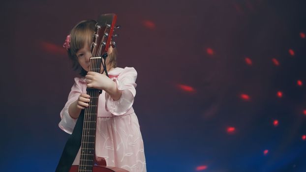 Little girl in a pink vintage dress plays an acoustic guitar like a double bass