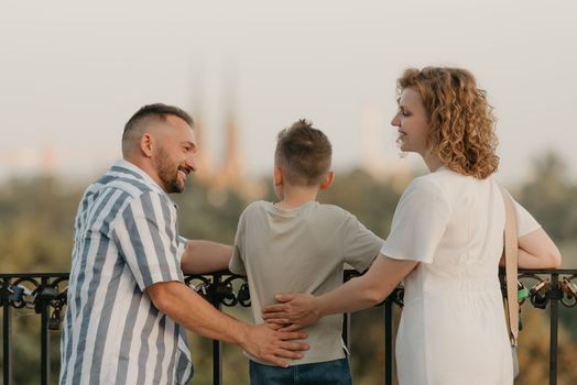 A photo from the back of father, mother, and son who are staring at the old European church. The happy family of tourists is enjoying the town sight in the evening. Tourists at sunset.