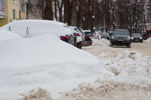 A large snowdrift against the backdrop of a city street with cars.