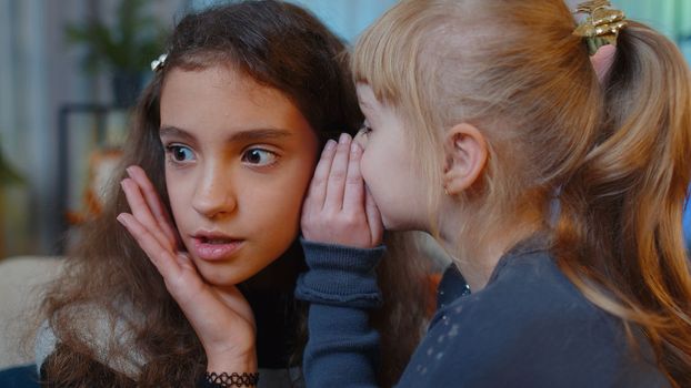Teenage child whisper news rumors in ear to little sister kid girl share secrets gossip having fun