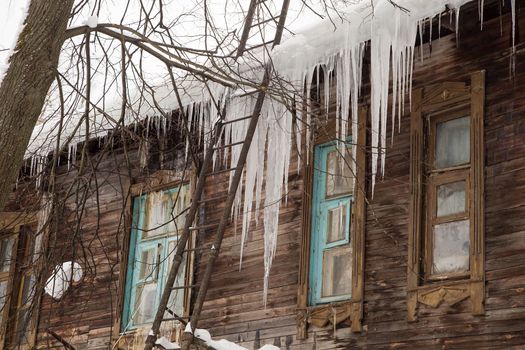 Sharp, frozen icicles hang on the edge of the roof, winter or spring