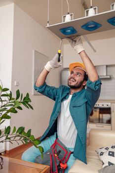 Professional electrician worker in uniform is installing electric lamps light in kitchen