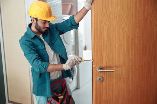 Locksmith workman in uniform installing door knob. Professional repair service
