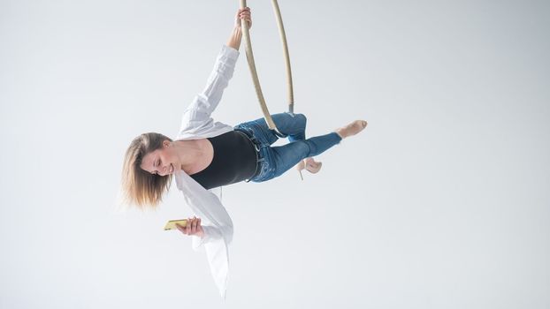 Caucasian female gymnast doing aerial hoop exercises and using smartphone.
