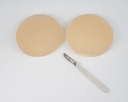 Breast silicone implants and a disposable scalpel on a white background.