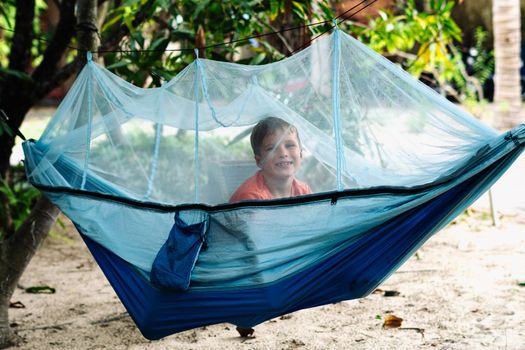 Smile child boy lie rest hammock with mosquito net. Happy childhood daydream. Look at from, laughing, portrait