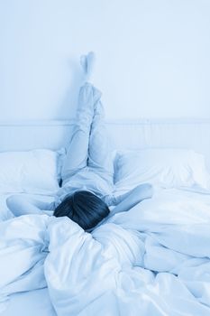 Woman wearing pajamas with legs raised up high and arms under her head lying on bed