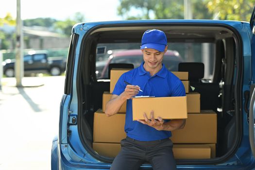 Image of delivery man sitting in open delivery van and checking checking address details of client on clipboard