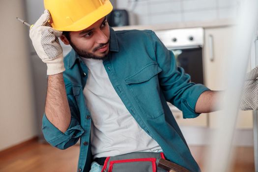 Focused professional worker in uniform is assembling furniture on kitchen. Repair concept