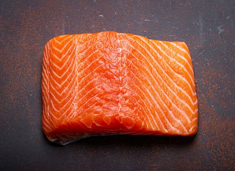 Piece of Norwegian raw salmon fillet on dark brown rustic background top view, healthy nutrition and diet