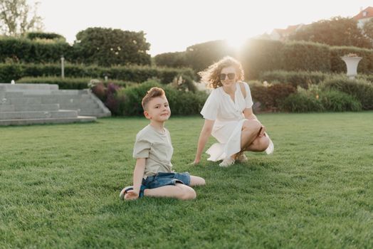 Mother and son are having fun in the garden of an old European town. Happy family in the evening. A boy is showing somersaults to his parent at sunset.