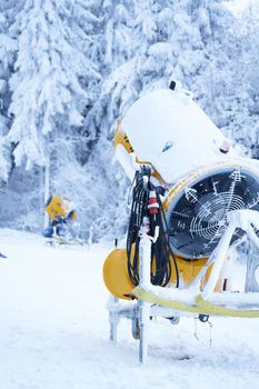 Yellow artificial snow cannon under snow on Wasserkuppe in Rhoen Hesse Germany ski resort on snowy mountain after fresh snow fall.