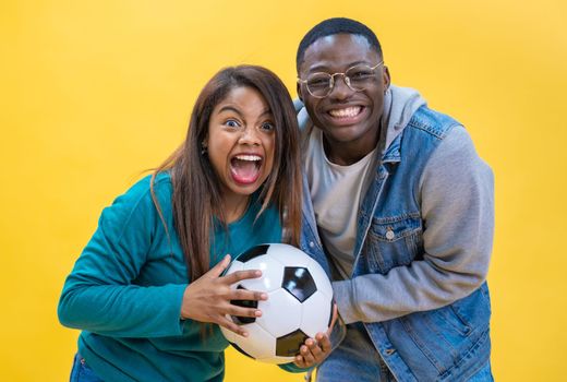 Excited ethnic diversity couple enjoying soccer together isolated on yellow background happy.