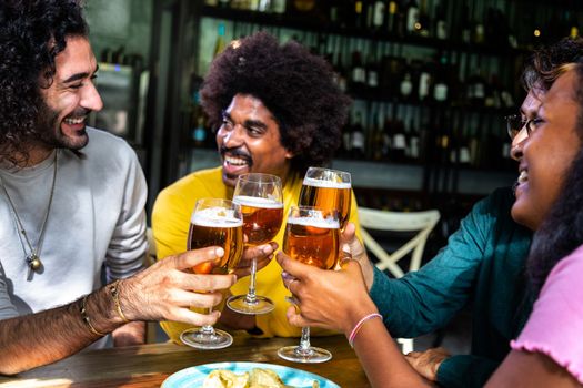 Multiracial happy friends enjoying drinks at a bar toasting, celebrating with beer.