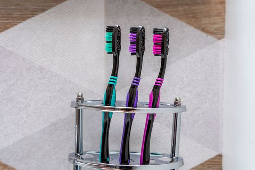 three multi-colored toothbrushes stand in a special stand in the bathroom interior. close-up. daily oral hygiene products