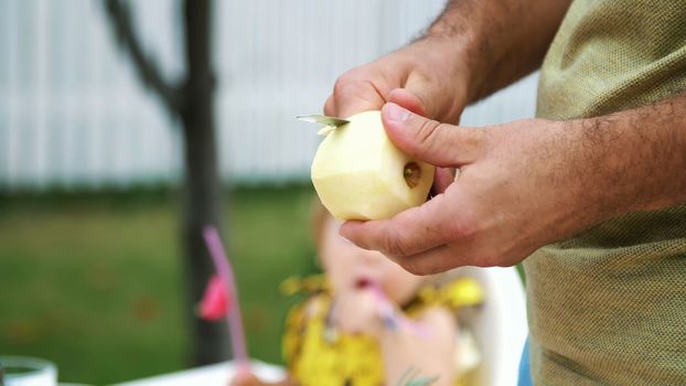 summer, in the garden, slow motion, close-up, men's hands, peel an apple with a knife, cut the peel.