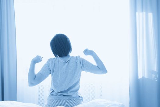 Woman stretching in bed after wake up in front of window, back view