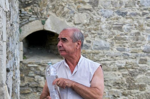 Elderly male pensioner with a bottle of mineral water on a tour in the old town