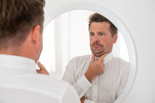 young man with a double chin examing his reflection in mirror