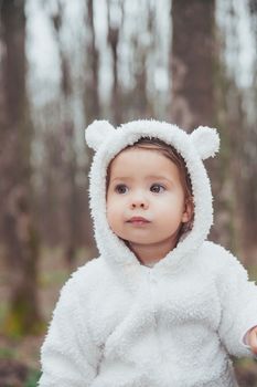 Adorable baby in a bear costume in the forest by a fallen tree